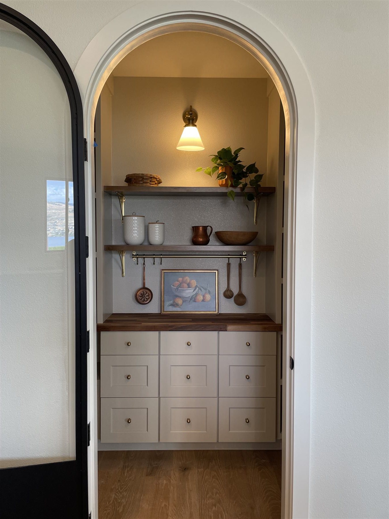 Styled arched pantry nook with open shelving and brass sconce