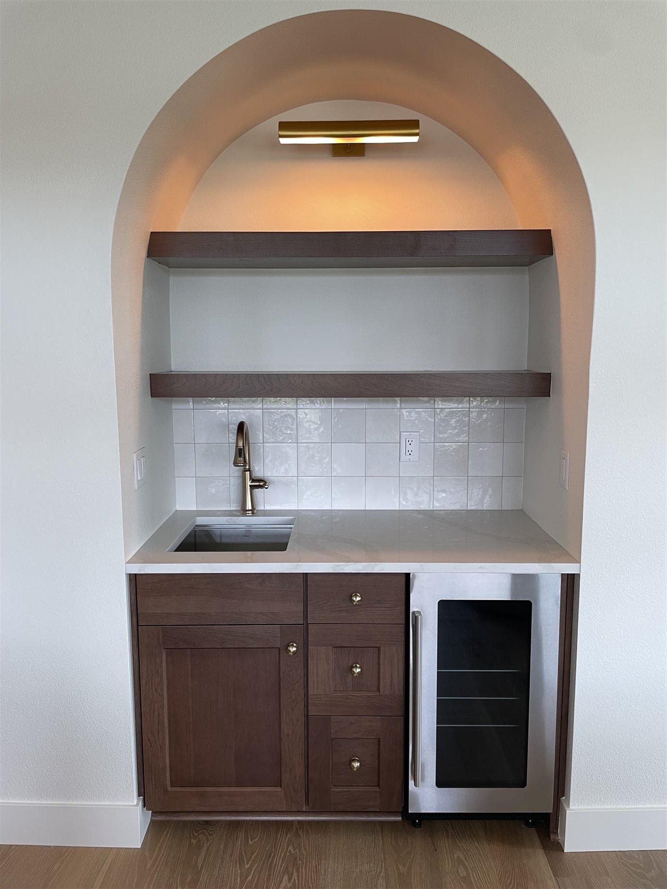 Arched wet bar nook with floating shelves, tile backsplash, and built-in wine fridge