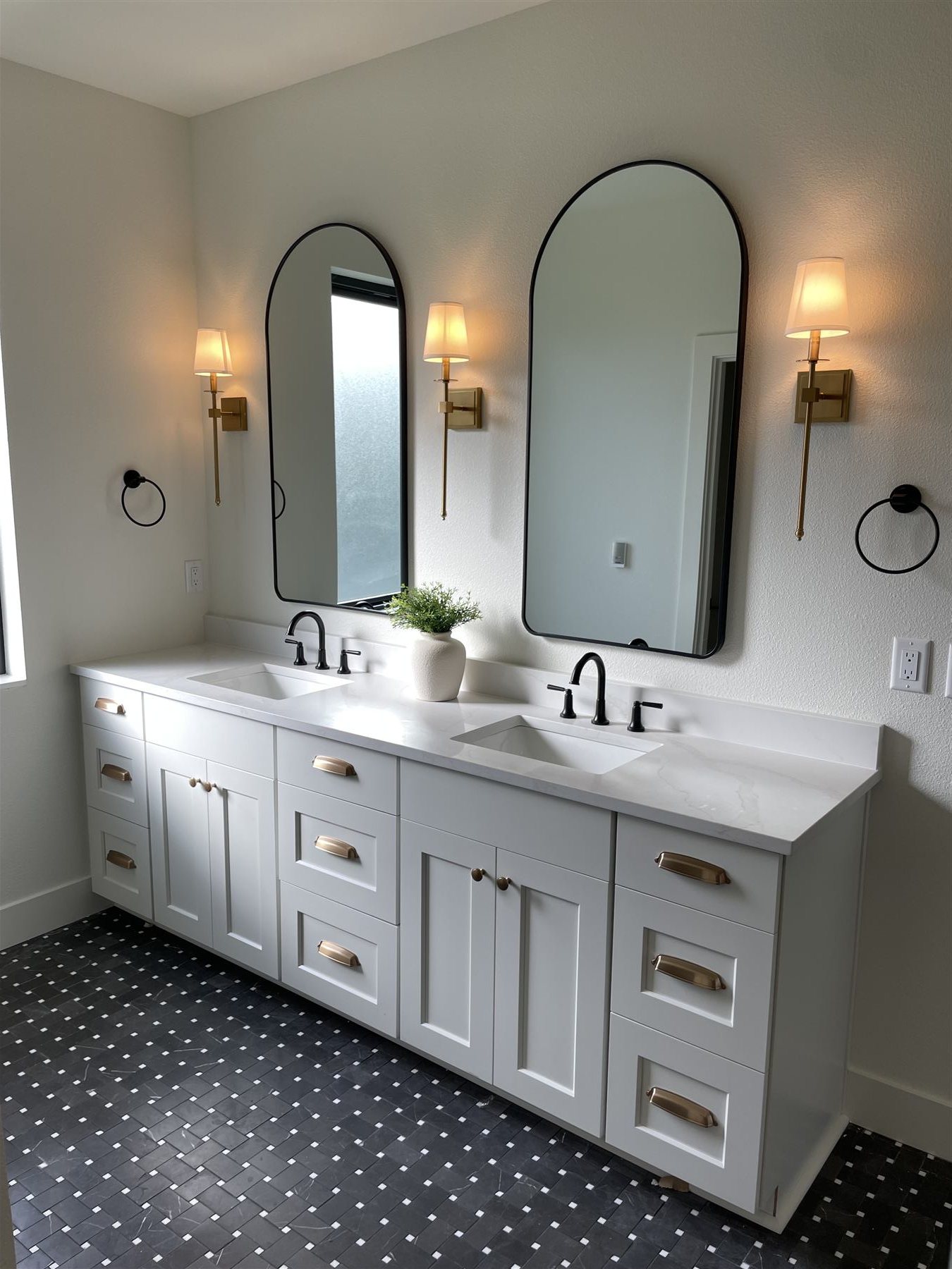Primary bath with twin arched black-framed mirrors over a white double vanity and mosaic floor
