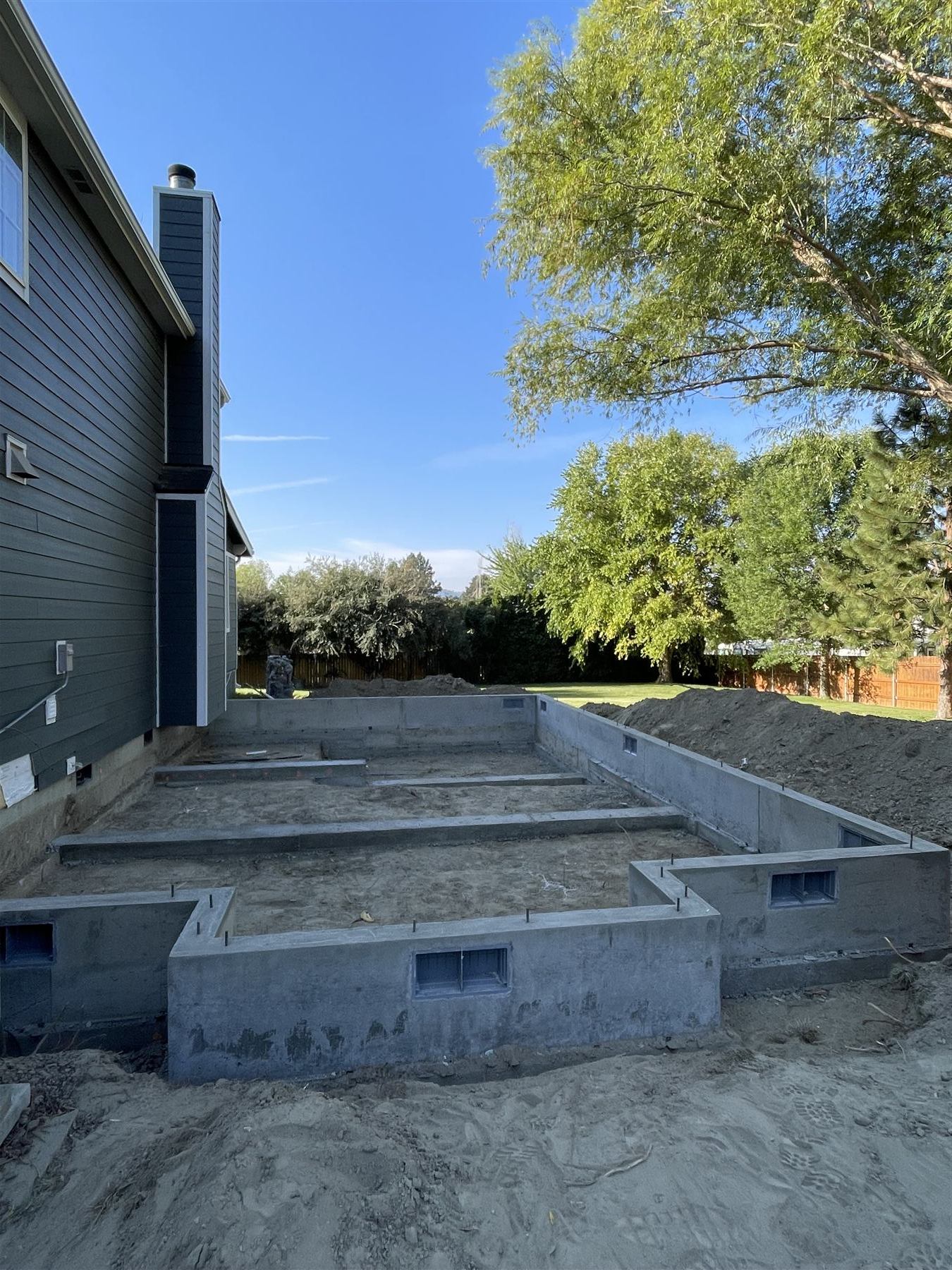 Poured foundation for a home addition with egress window wells, attached to an existing house