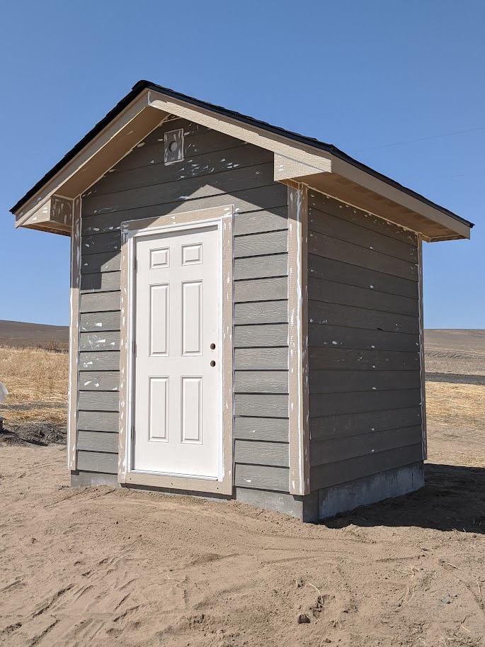 Finished small storage shed with gray siding and a white door